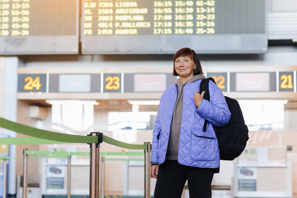 Mulher de meia-idade viajante com mochila no terminal do aeroporto público após o check-in em balcões de serviços da companhia aérea. Reformados activos. Viajar, férias, conceito de turismo - Foto, Imagem