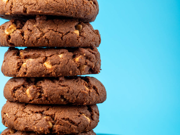 Σοκολατένια, πλούσια μπισκότα με αντιθέσεις σε μάρκες λευκής σοκολάτας σε μπλε φόντο. Cookies με λευκή σοκολάτα close-up. - Φωτογραφία, εικόνα