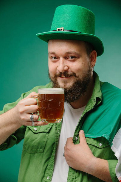 暗い緑の背景にビールとアイルランドの旗のグラスを持つ幸せなひげ付き男. 聖パトリックの日. - 写真・画像