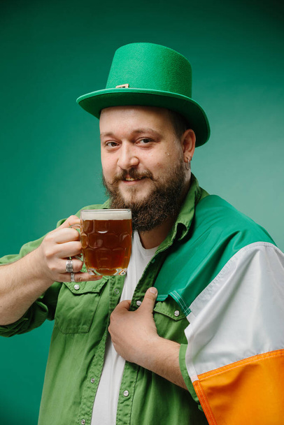 Onnellinen parrakas mies, jolla on lasi olutta ja Irlannin lippu tummanvihreällä pohjalla. Pyhän Patrickin päivä. - Valokuva, kuva