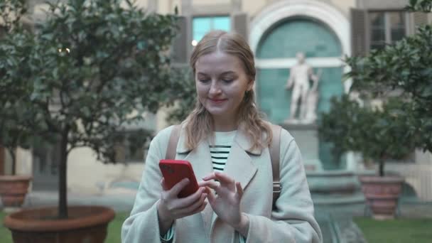 Sahilde cep telefonu kullanıp gülümseyen Kafkasyalı bir turist kadın. Gezgin kadın kameraya gülümsüyor Floransa, Toskana, İtalya 'daki Palazzo Medici Riccardi' nin bahçesinin keyfini çıkarıyor..  - Video, Çekim