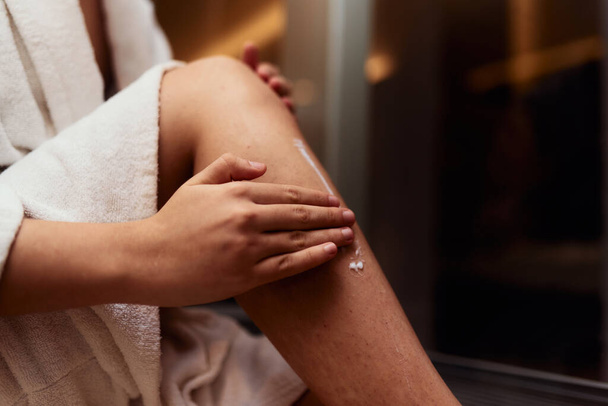Uma mulher se entrega à sua rotina de autocuidado, mimando sua pele após um banho relaxante, aplicando creme hidratante em suas pernas, abraçando a essência da beleza e bem-estar..  - Foto, Imagem