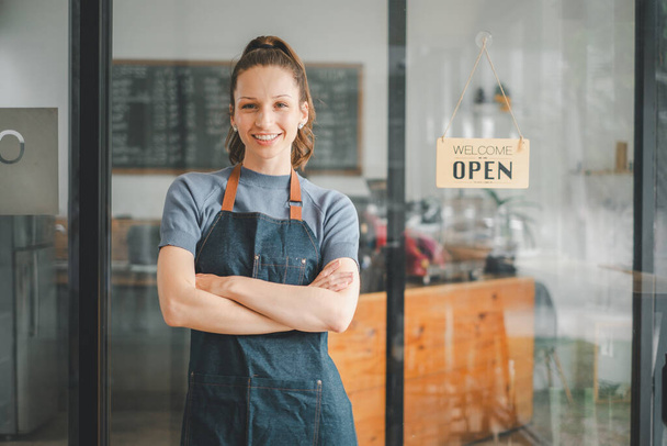 Restoran girişinde açık tabela ile duran mutlu garson portresi, genç iş kadınının portresi kahve dükkanındaki yeni müşterilere katılıyor.. - Fotoğraf, Görsel