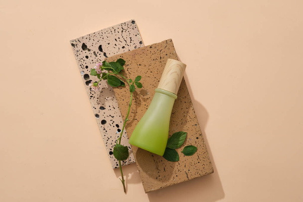 Top view of green glass bottle without label placed on two bricks on beige background. Mock up organic cosmetic with green leaves. Minimal style, space for design - Photo, Image