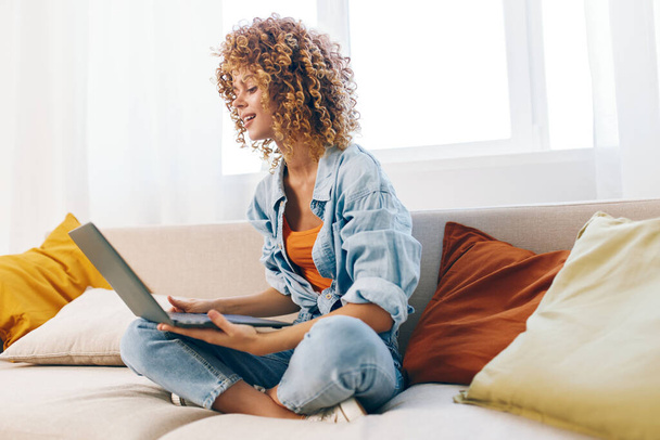 Usmívající se žena sedí na útulné pohovce, pracuje na moderním notebooku v pohodlné domácí kanceláři - Fotografie, Obrázek