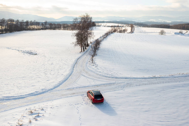 Κόκκινο αυτοκίνητο οδήγηση κάτω χιόνι καλύπτονται δρόμο, το χειμώνα ταξίδι μέσα από το τοπίο. - Φωτογραφία, εικόνα