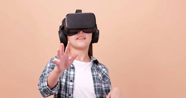 A girl having fun with game while wearing virtual reality glasses. Isolated on brown background in studio. - Photo, Image