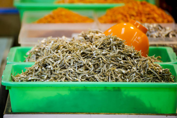  Ein grüner Plastikbehälter ist mit grauen kleinen Trockenfischen gefüllt - Foto, Bild