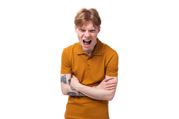 コピースペースのある白い背景で叫んでいるオレンジ色のTシャツの若い赤毛の男. - 写真・画像