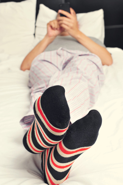 fiatal férfi az ágyban egy okostelefon segítségével - Fotó, kép