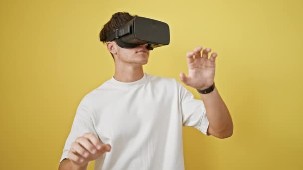 Joven adolescente hispano sonriente y confiado, felizmente inmerso en juegos de alta tecnología, usando gafas futuristas de realidad virtual sobre un vibrante fondo amarillo aislado - Imágenes, Vídeo