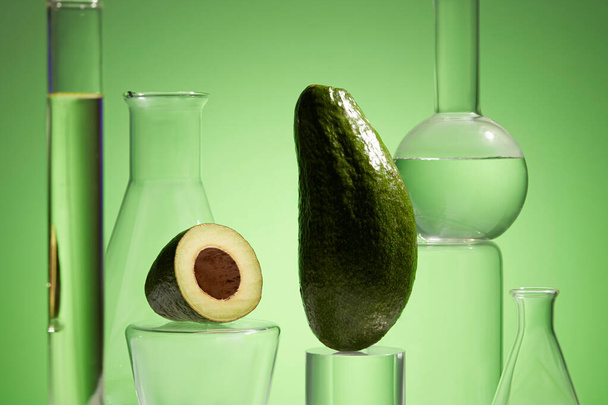 Fresh avocado and essential oil in lab glassware on green background. Research and development natural extract concept. Production of cosmetics based on avocado. - Photo, Image