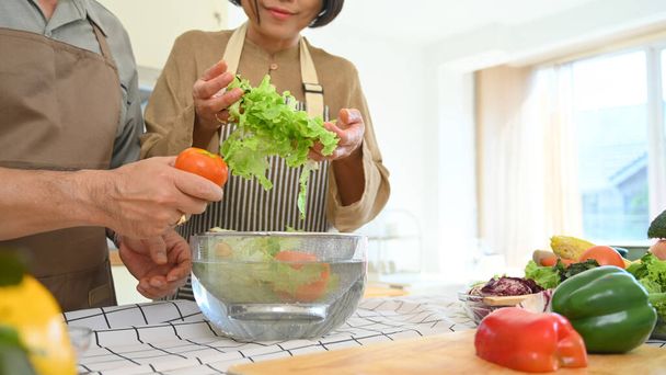 Ζευγάρι μέσης ηλικίας ετοιμάζει υγιεινό γεύμα με φρέσκα βιολογικά λαχανικά στην κουζίνα. Υγιεινός τρόπος ζωής και διατροφή των τροφίμων. - Φωτογραφία, εικόνα