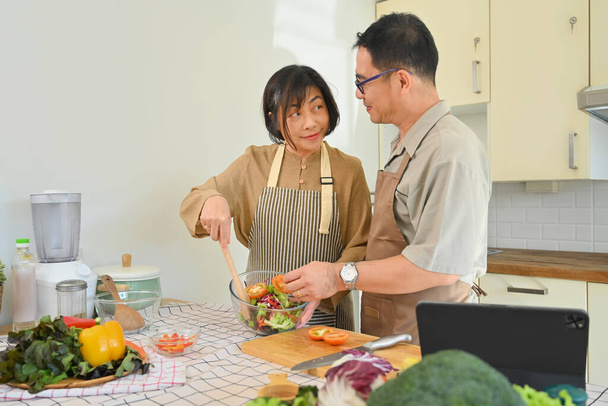 Tiro de um casal sênior feliz cozinhar vegan comida vegetariana refeição na cozinha. Conceito de alimentação saudável - Foto, Imagem