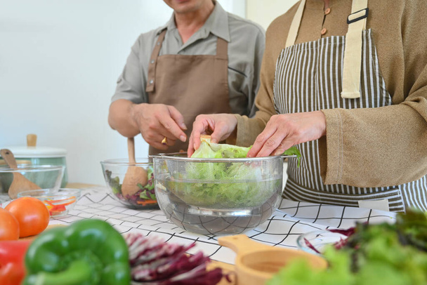 Gehakt schot middelbare leeftijd paar het bereiden van gezonde maaltijd met verse biologische groenten in de keuken. - Foto, afbeelding