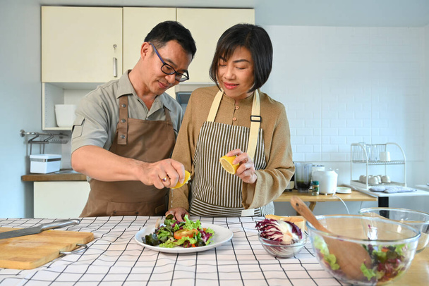 Middle age couple preparing healthy vegetables salad in kitchen. Happy senior lifestyle concept - Photo, Image
