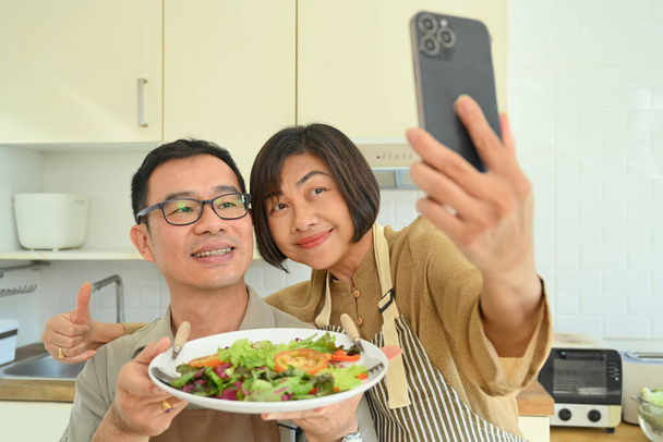Mutlu son sınıf çifti mutfakta yemek hazırlarken selfie çekiyor. - Fotoğraf, Görsel