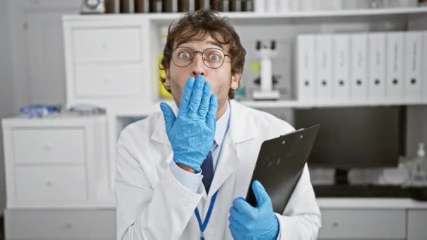 Schockierter junger Wissenschaftler bedeckt Mund mit Hand, Überraschung steht ihm ins Gesicht geschrieben! Betäubender Schnitzer schürt Angst im Labor. - Filmmaterial, Video