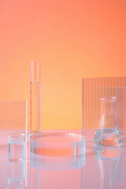 Laboratuvar camları renksiz sıvı ve turuncu arka planda tırtıklı akrilik çarşaflarla şeffaf podyumun ön görüntüsü. Ekran ürünü için boş alan. Bilim ve tıp geçmişi - Fotoğraf, Görsel