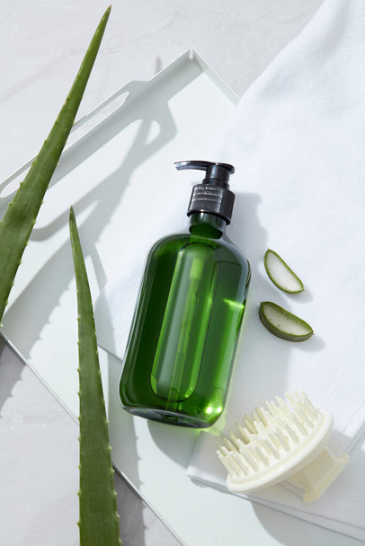 Mockup pro šampon produkt se zelenou lahví neoznačené, hřeben, ručník a čerstvé aloe vera na bílém pozadí. Aloe vera obsahuje mnoho aminokyselin a proteolytických enzymů, vitamíny, které jsou dobré pro vlasy - Fotografie, Obrázek