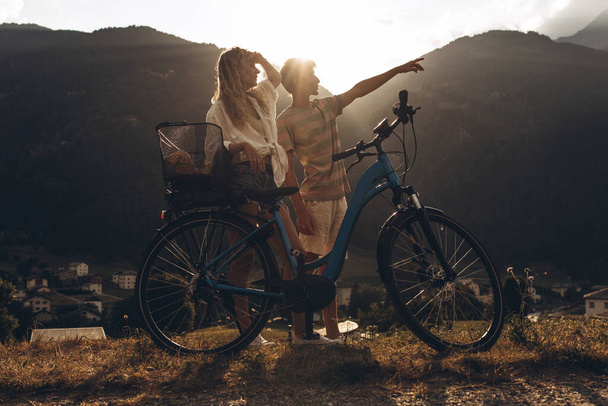 Two friends or couple are cycling along the road. Sport and active life sunset time concept. Couple learning to ride a bike, having fun together, traveling in the mountains near the city - Photo, Image