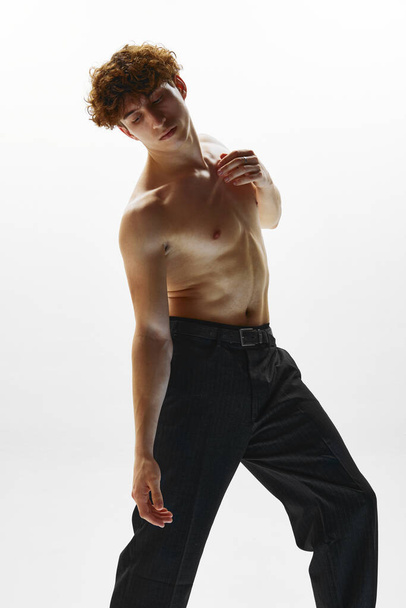 Photo of athletic man, ballet dancer dressed in black trousers making dance elements against white studio background. Beauty and art, motion, action, flexibility, inspiration concept. - Photo, Image