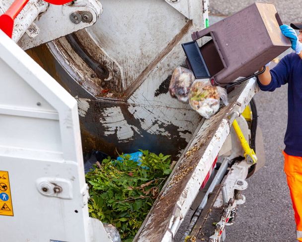 Ekologinen työntekijä tyhjentää ämpärillisen orgaanista jätettä roska-autoon. - Valokuva, kuva