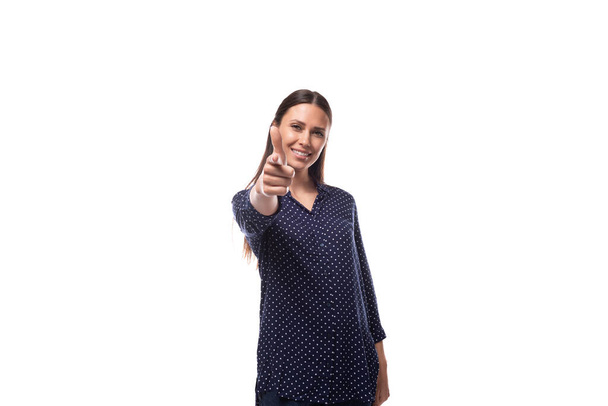 νεαρή μελαχρινή διαφημίστρια γυναίκα ντυμένη με μπλε μπλούζα με πουά μοτίβο φαίνεται χαρούμενη και χαρούμενη σε λευκό φόντο με αντίγραφο χώρου. - Φωτογραφία, εικόνα
