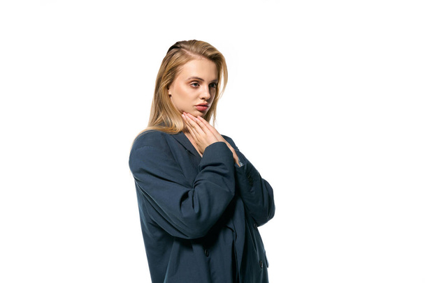 όμορφη ξανθιά γυναίκα σε κομψό μπλε σακάκι ποζάρουν σε λευκό φόντο και κοιτάζοντας μακριά - Φωτογραφία, εικόνα