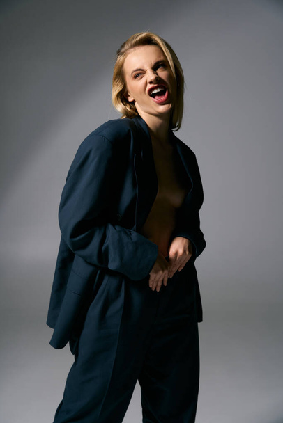 alegre hermosa sexy mujer en azul desabrochado chaqueta posando sobre fondo gris y mirando hacia otro lado - Foto, imagen