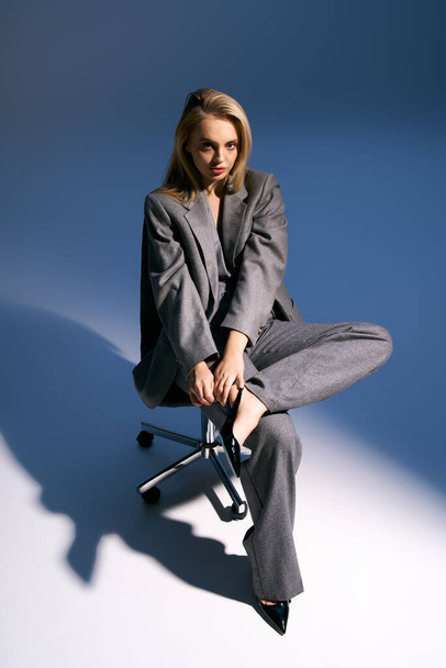 attraktive junge Frau im eleganten silbernen Smoking mit blonden Haaren sitzt auf einem Stuhl und schaut weg - Foto, Bild