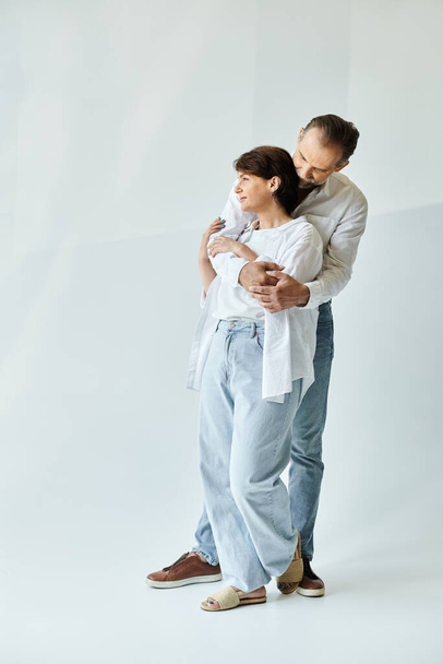 グレーの背景と抱擁に立っている成熟した美しいカップルの完全な長さのショット - 写真・画像