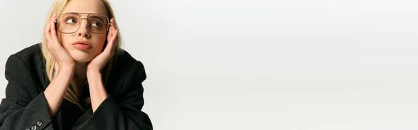graziosa giovane donna con capelli biondi e occhiali chic in cappotto nero in posa e distogliendo lo sguardo, banner - Foto, immagini