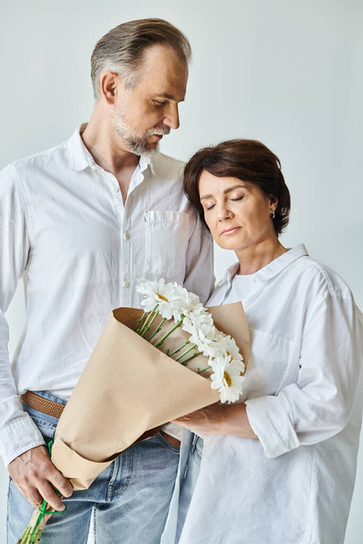 Portret van volwassen man in wit shirt presenteren bloemen aan een aantrekkelijke vrouw op grijze achtergrond - Foto, afbeelding