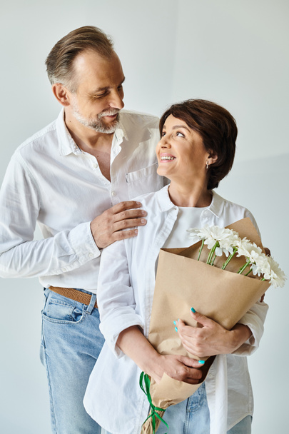 Портрет улыбающейся зрелой пары, стоящей вместе с цветами на сером фоне - Фото, изображение