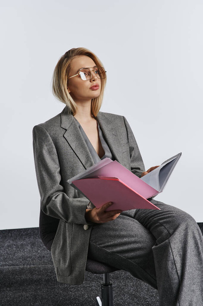 debonair femme d'affaires à la mode en costume gris intelligent avec des lunettes de travail avec sa paperasse - Photo, image