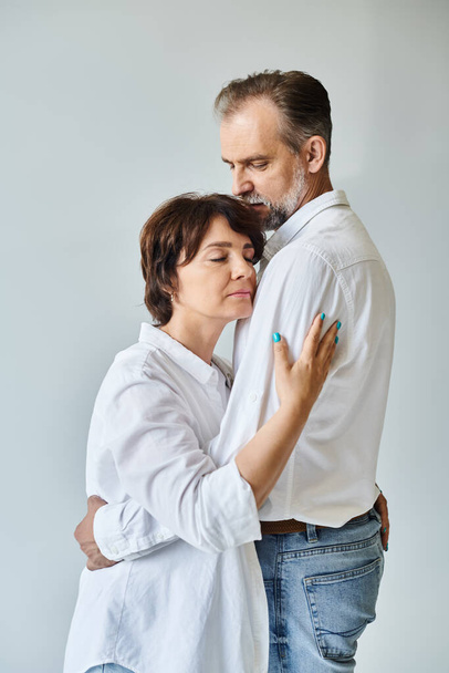 Attractive middle aged woman hugging mature man in white shirt with love on grey background - Photo, Image