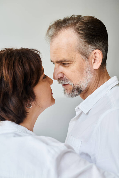 Side view portrait of mature couple in love hugging and going to kiss on grey backdrop, closeness - Photo, Image