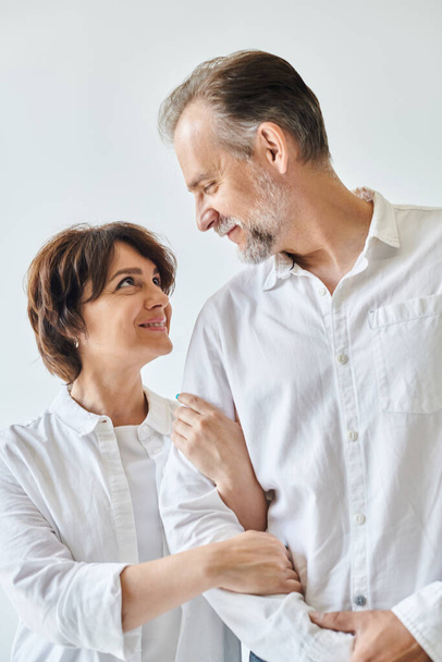 Attractive middle aged woman hugging mature man in white shirt with love on grey background - Fotó, kép