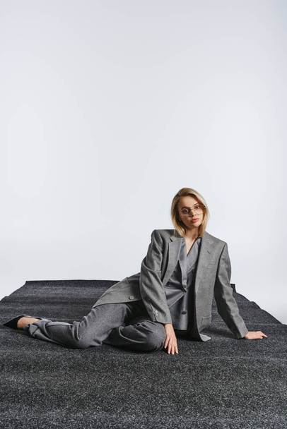 mujer elegante de moda con gafas con estilo en traje elegante sentado en el suelo y mirando a la cámara - Foto, Imagen