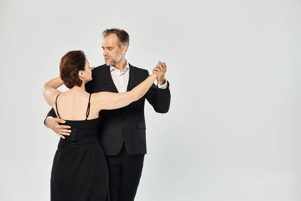 Portrait de couple séduisant d'âge moyen dans une pose de danse tango isolé sur fond gris - Photo, image