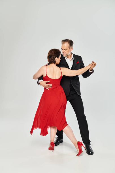 In voller Länge Bild von reifen attraktiven Paar in rotem Kleid und Anzug tanzen auf grauem Hintergrund - Foto, Bild