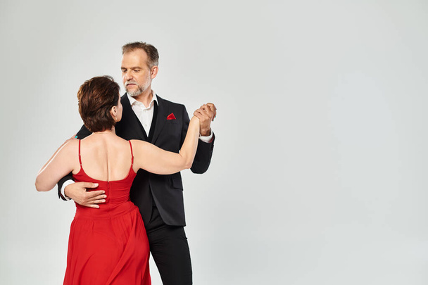 Середнього віку приваблива пристрасна пара танцює бальний танець ізольовано на сірому фоні - Фото, зображення