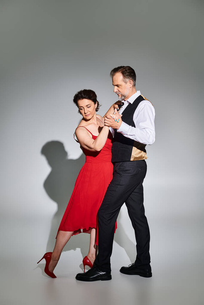 Ballroom dance middle aged couple in red dress and suit dancing tango isolated on grey background - Fotó, kép