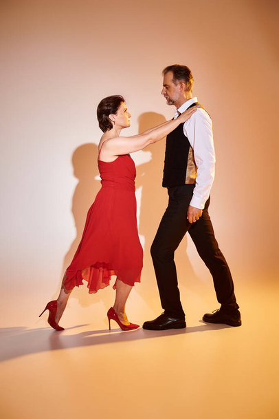 Image of mature couple tango dancers in red dress and suit performing on grey background - Photo, Image