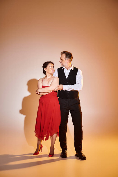 Portrait of middle aged attractive couple in red dress and suit standing on grey background - Foto, Imagem