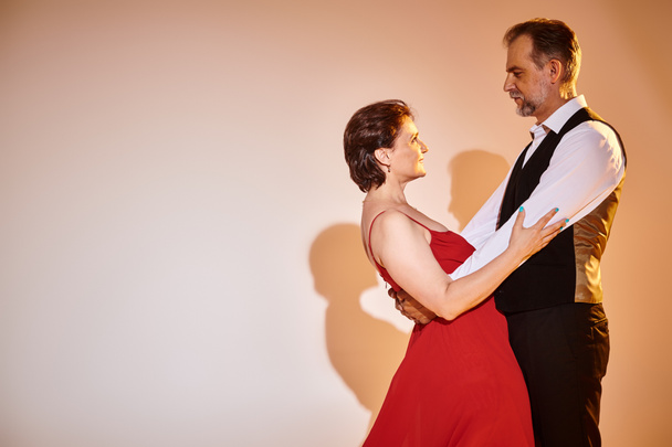 Side view of mature attractive smiling couple dancing ballroom dance isolated on grey background - Fotó, kép