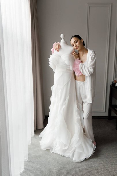 朝とパジャマとランジェリーの豪華な部屋で豪華で美しい花嫁のための準備,靴とシックな白のウェディングドレスを着る. - 写真・画像