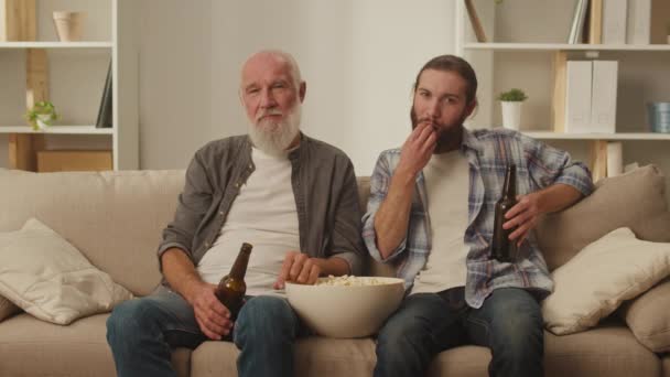 Старшие и молодые друзья на диване, с попкорном в руках, участвуют в просмотре живых фильмов, общении поколений, приятных семейных моментов, наблюдая вместе - Кадры, видео