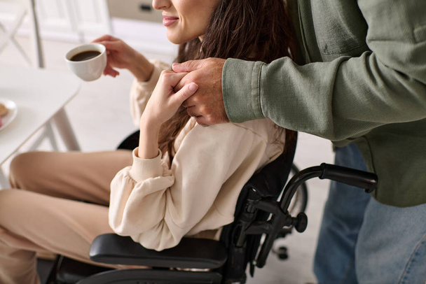 обрезанный вид веселой женщины-инвалида в инвалидной коляске, пьющей кофе с мужем за завтраком - Фото, изображение